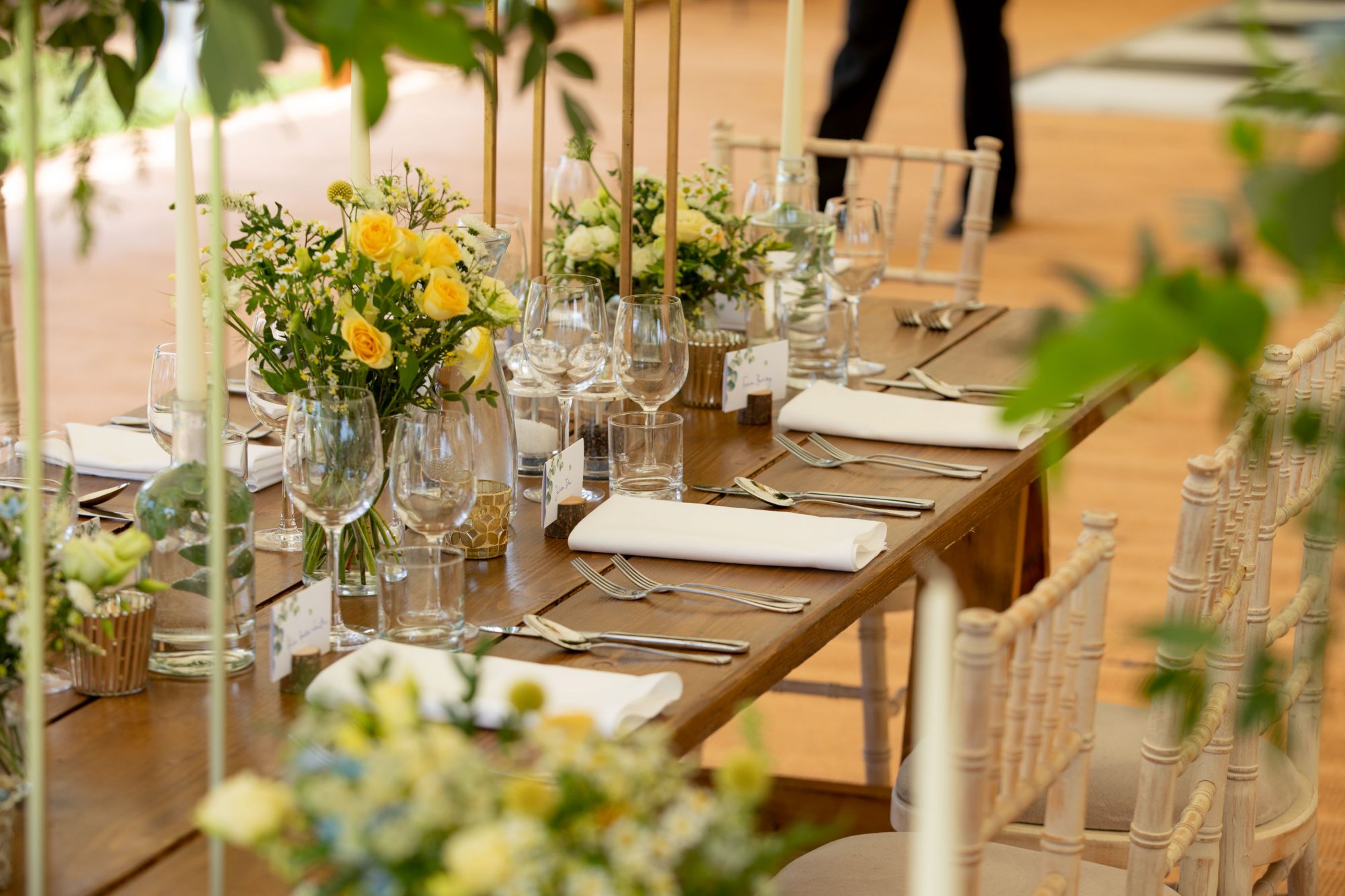 Wide rustic wooden trestle tables with botanical theme, white pillar candles and ivory crockery